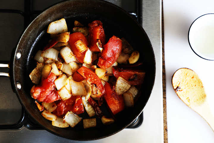 Browned tomatoes, onion, and garlic in pan on stove.