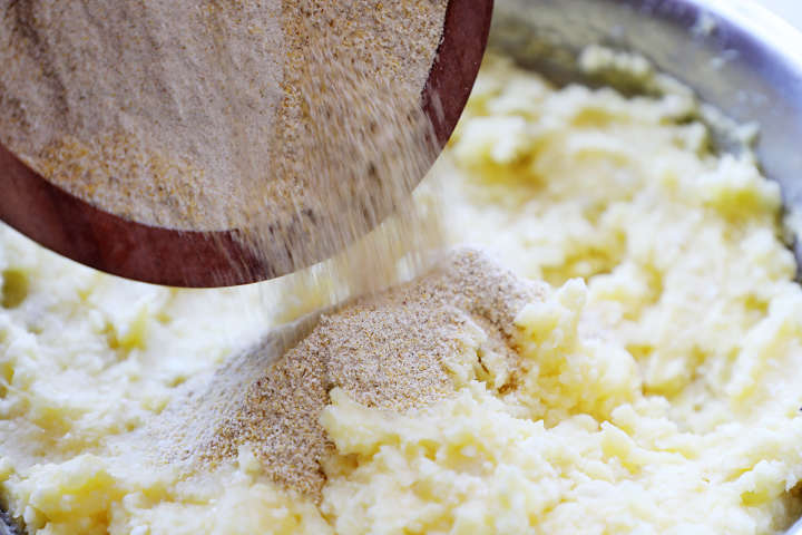 Adding breadcrumbs to potato, egg, and cheese mixture.