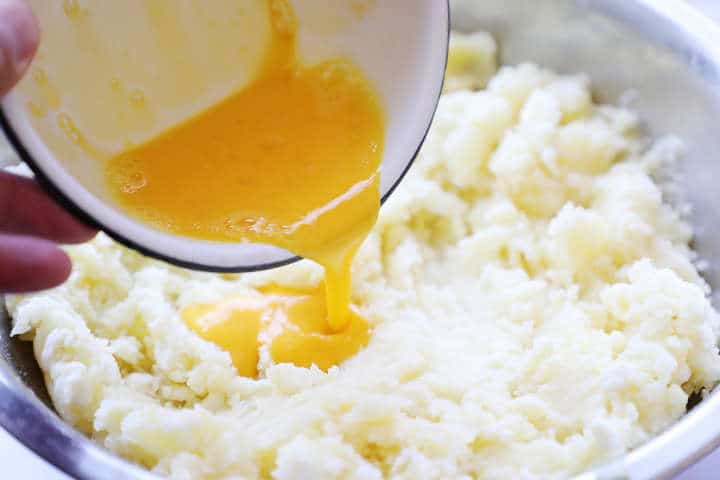 Adding beaten egg to potato cheese mixture in mixing bowl.