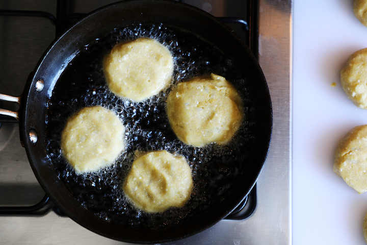 Four potato croquettes frying in pan.