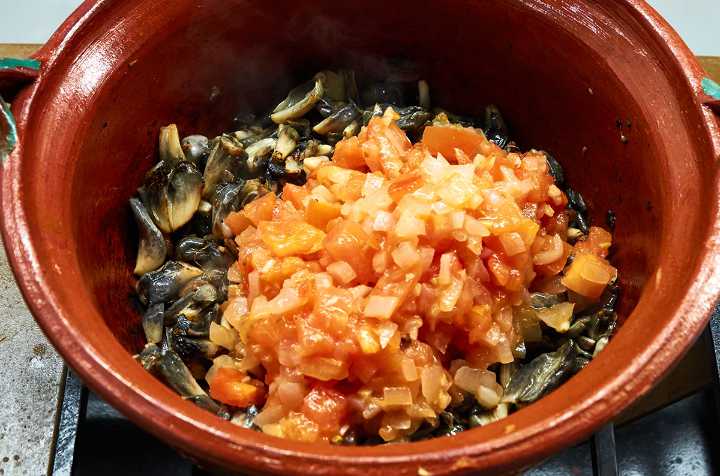 Tomatoes, onions, huitlacoche in clay pot on stove.