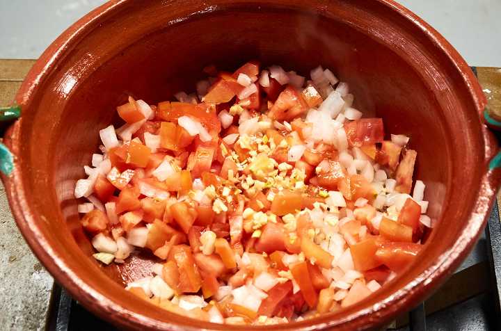 Chopped onion, tomato, and garlic in pot on stove.