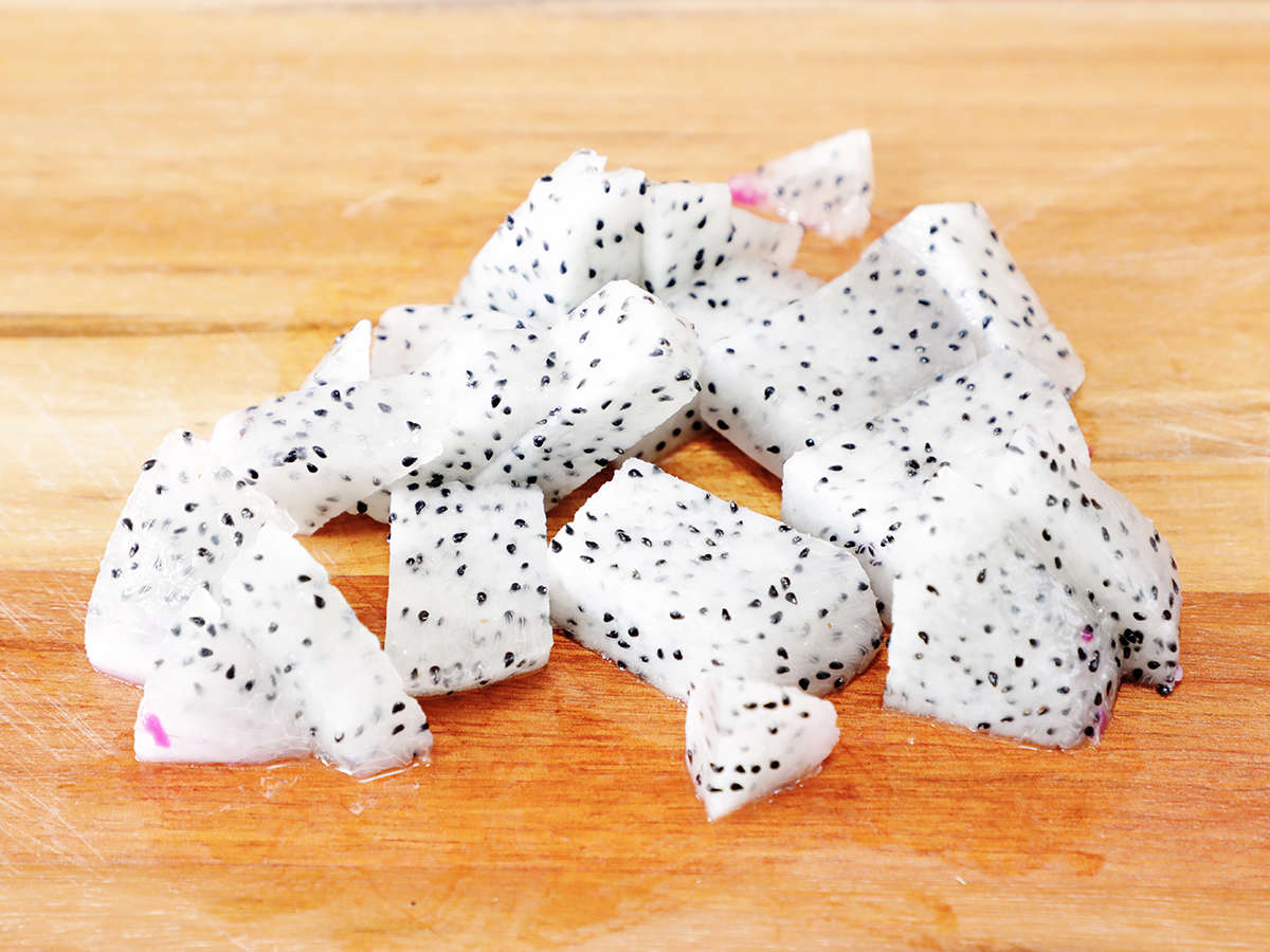 Chunks of dragon fruit on wooden cutting board.