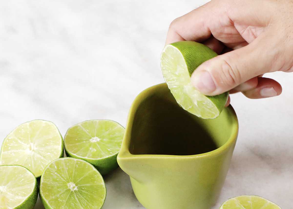 Squeezing lime juice into a small ceramic pitcher.